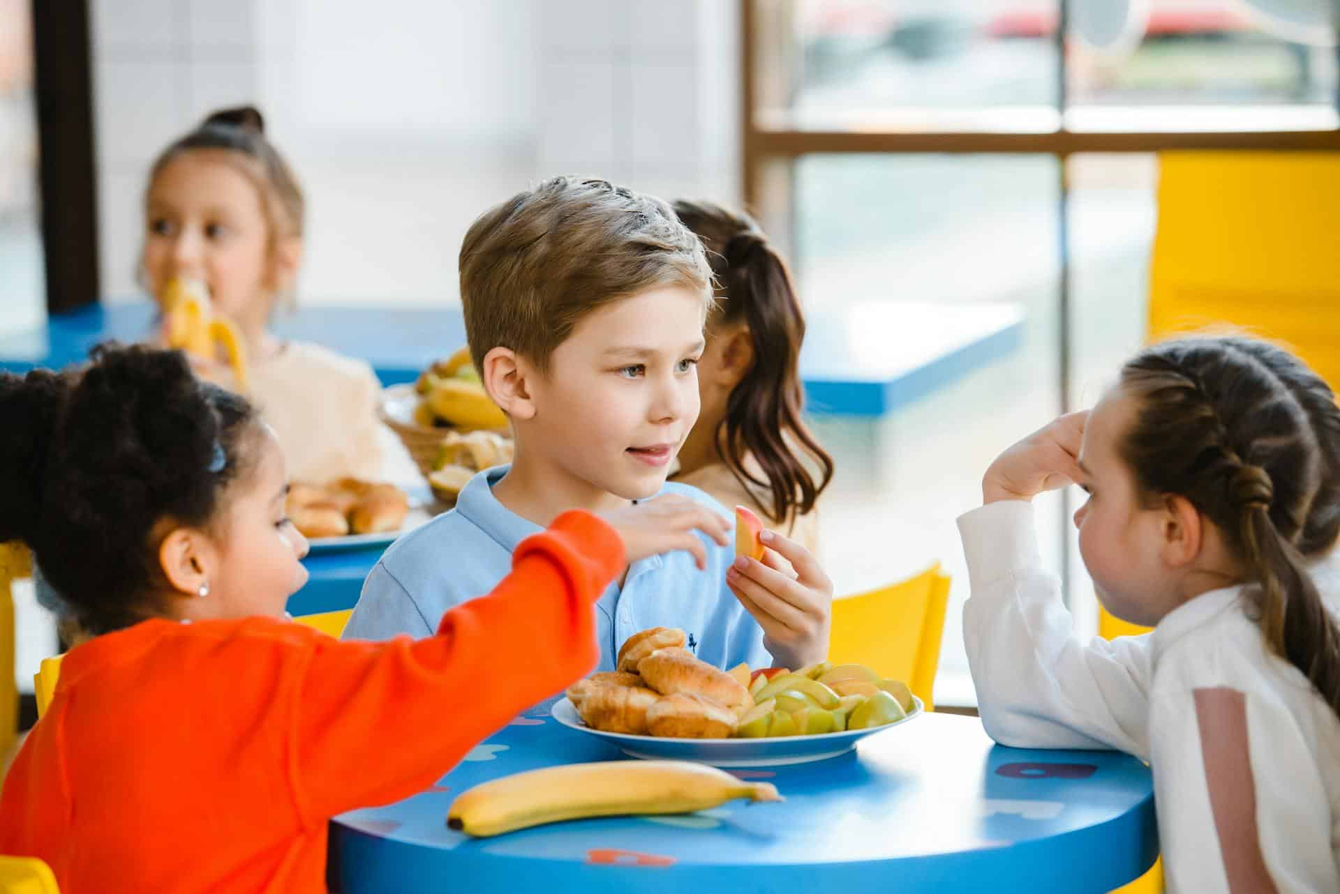 Bambini che mangiano il pasto scolastico in mensa con amici.